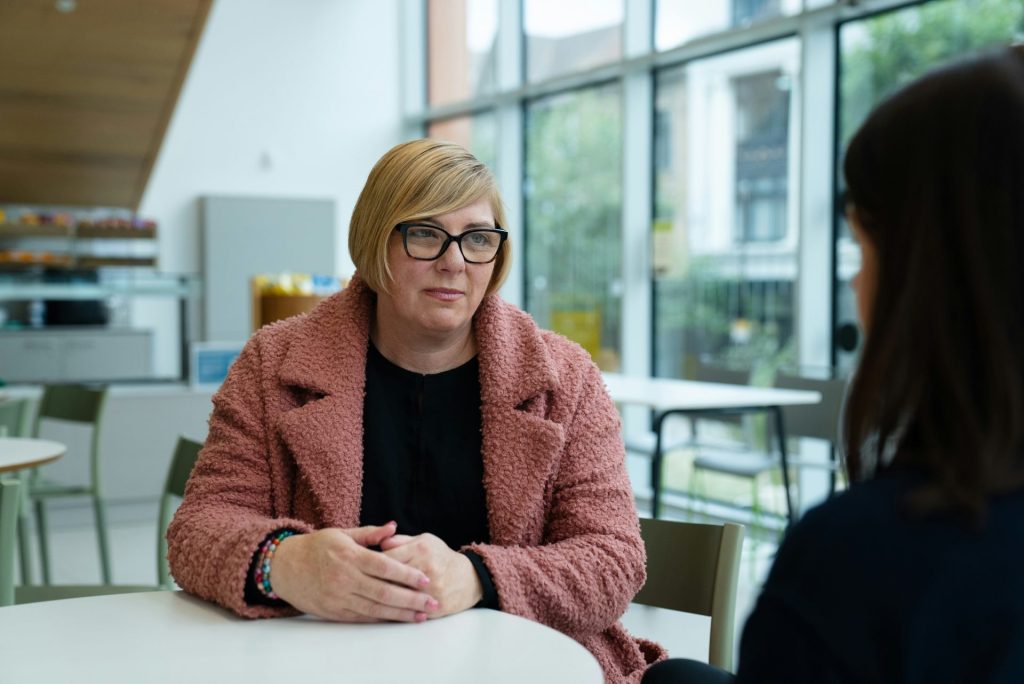 Une femme en manteau rose parle à quelqu'un à table